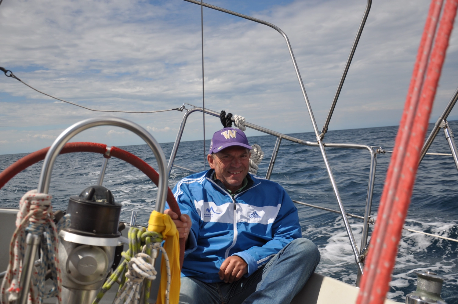 Motorboot-u. Segelschule Ravensburg - Wassersportausbildung und lizenzierung - Ein Mann mit einer lila Baseballkappe sitzt am Steuer eines Segelboots auf dem offenen Meer.